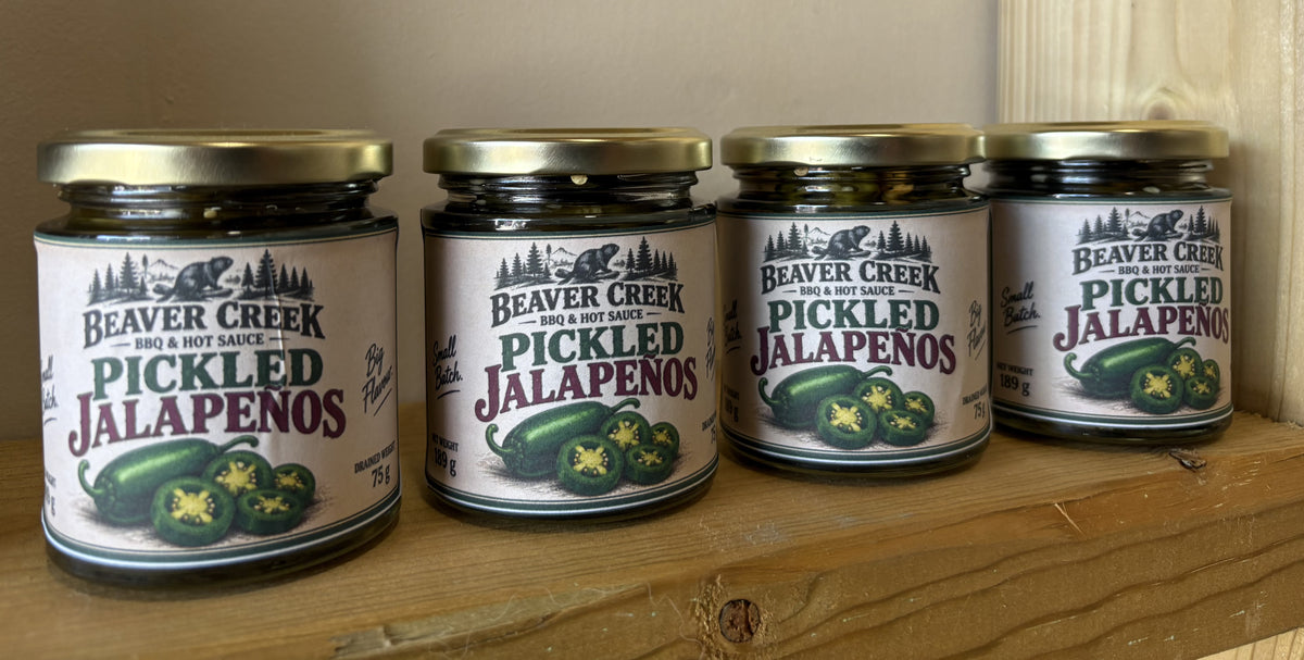 Four jars of Beaver Creek Pickled Jalapeños lined up on a wooden shelf